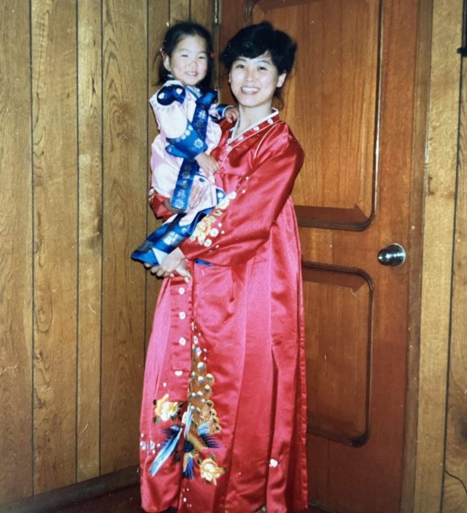 Young woman wearing a long red festive Asian dress holding in her arms a young child, also in festive clothing.